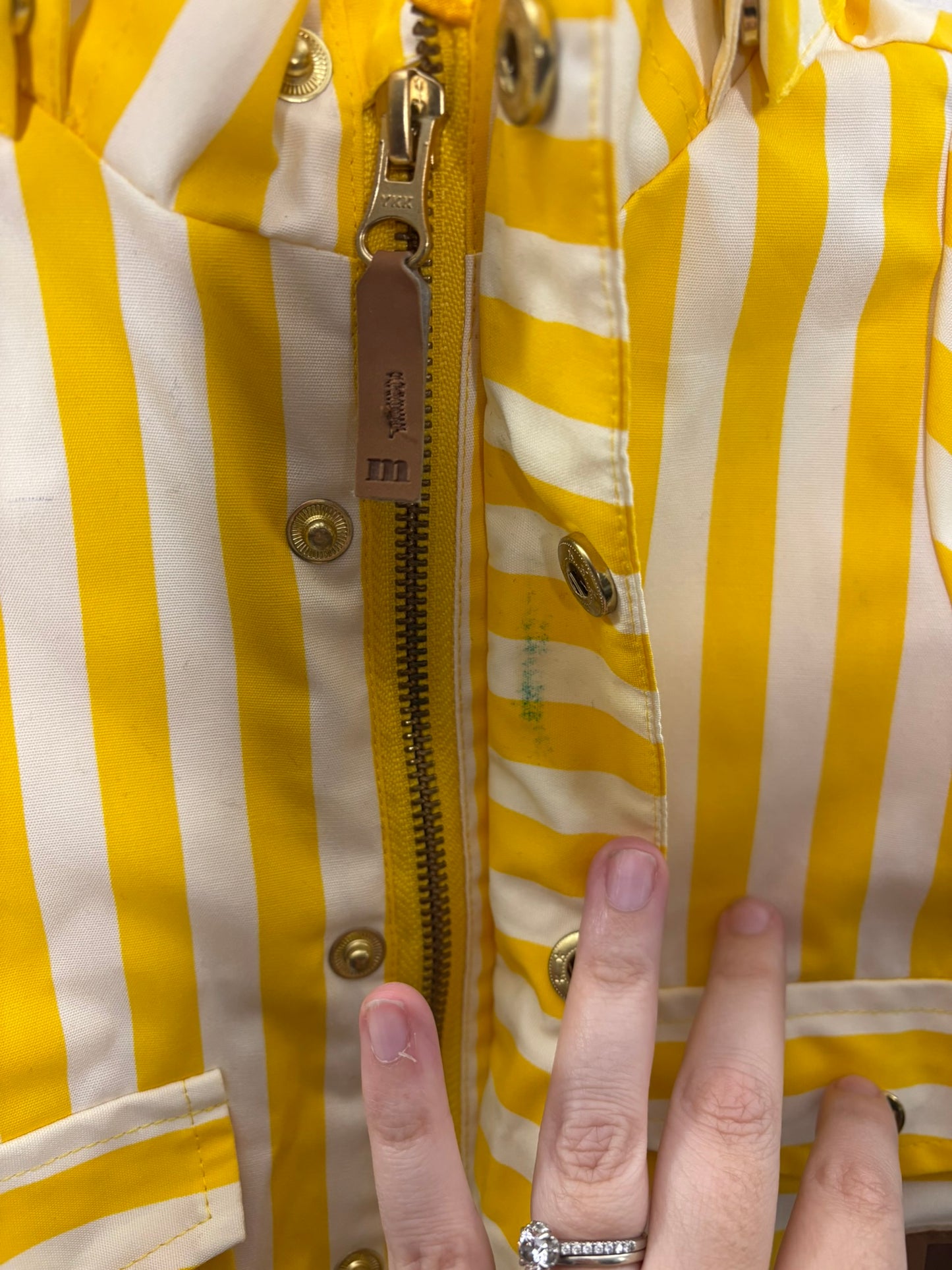 Yellow and white striped hooded raincoat for kids, featuring buttons and front pockets, hanging against a brick wall.