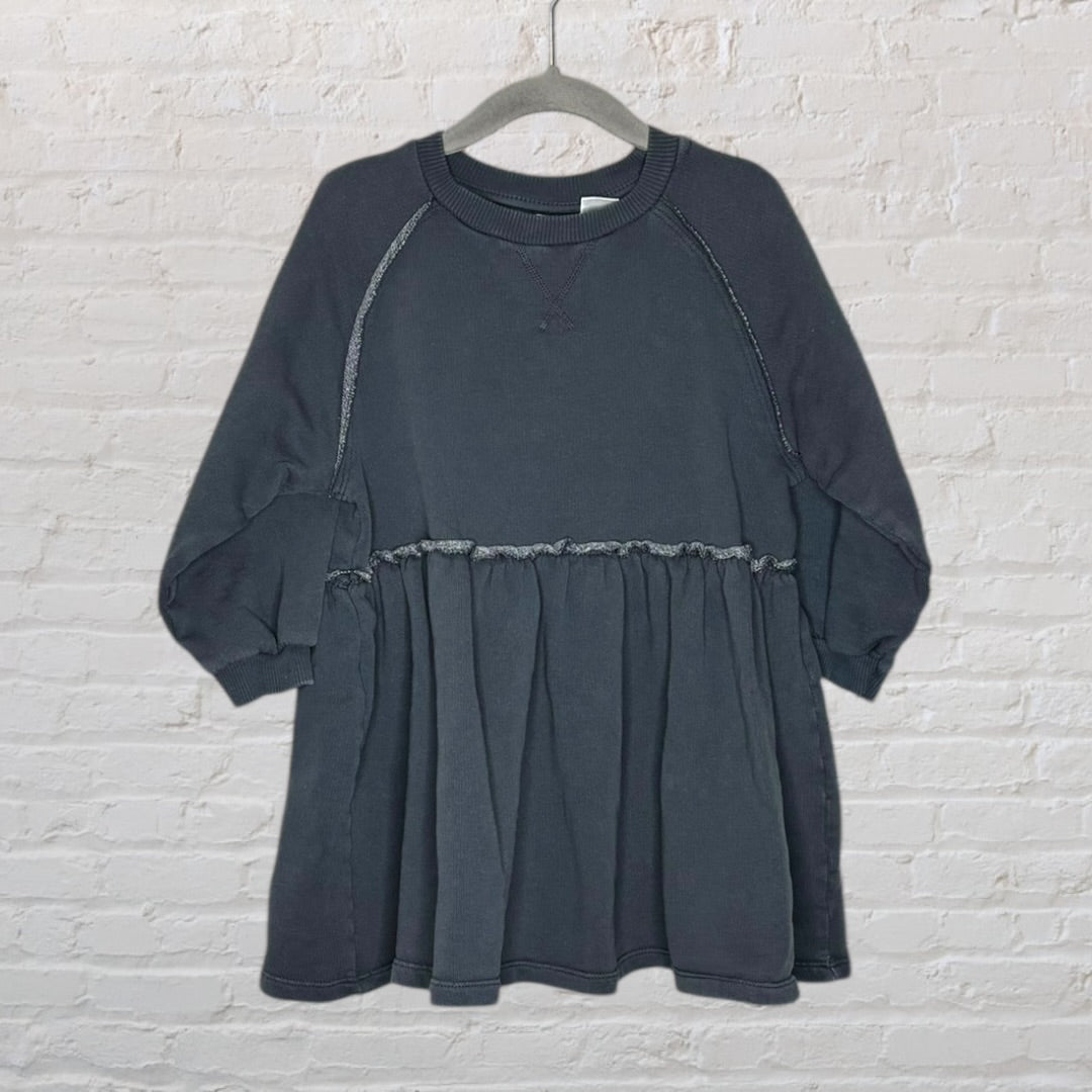 Dark grey raglan sleeve dress with a gathered waist and ribbed neckline, displayed on a hanger against a brick wall.