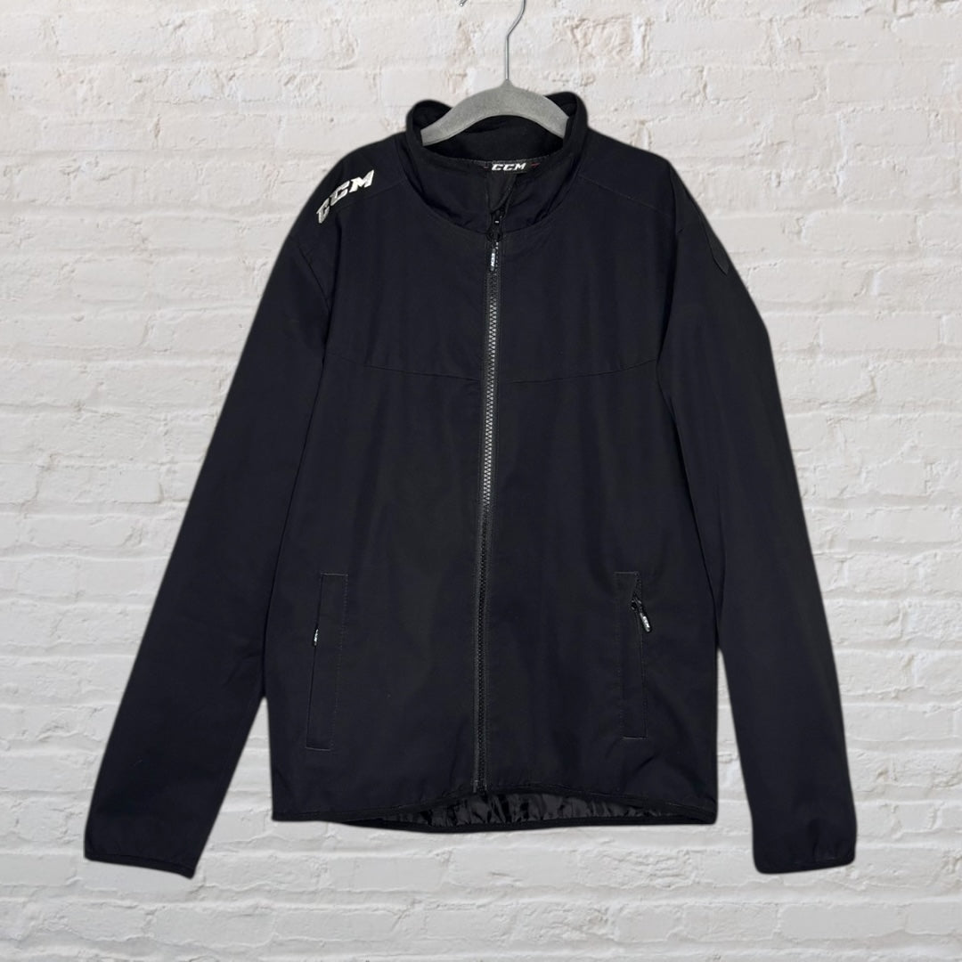Black CCM full zip jacket with two zippered pockets and logo on the shoulder, displayed on a hanger.
