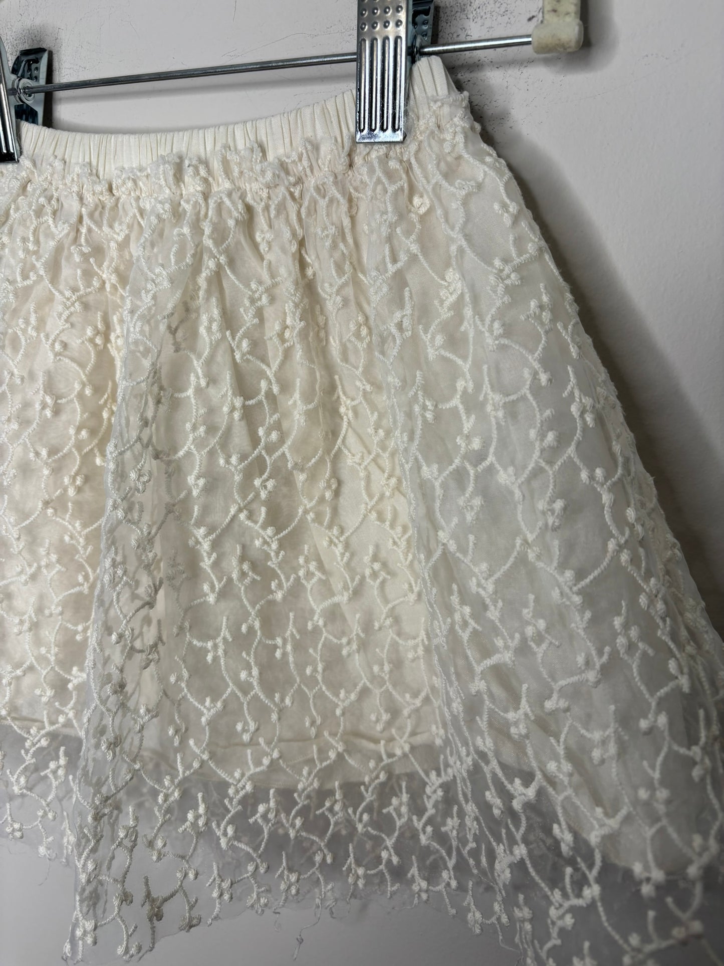 Cream skirt with lace overlay design hanging against a brick wall.