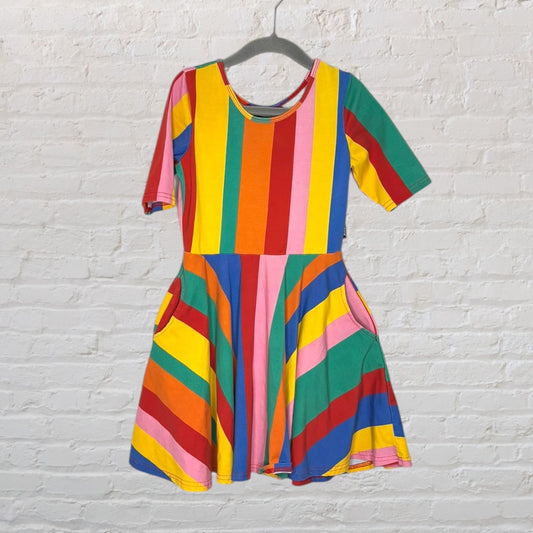 Vibrant rainbow-striped short sleeve dress with a fitted top and flared skirt, hanging on a hanger against a white brick wall.