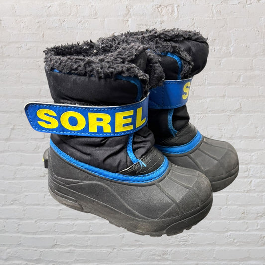 Pair of Sorel winter, snow boots in black with blue trim and yellow logo, featuring a rubber sole and fuzzy lining.