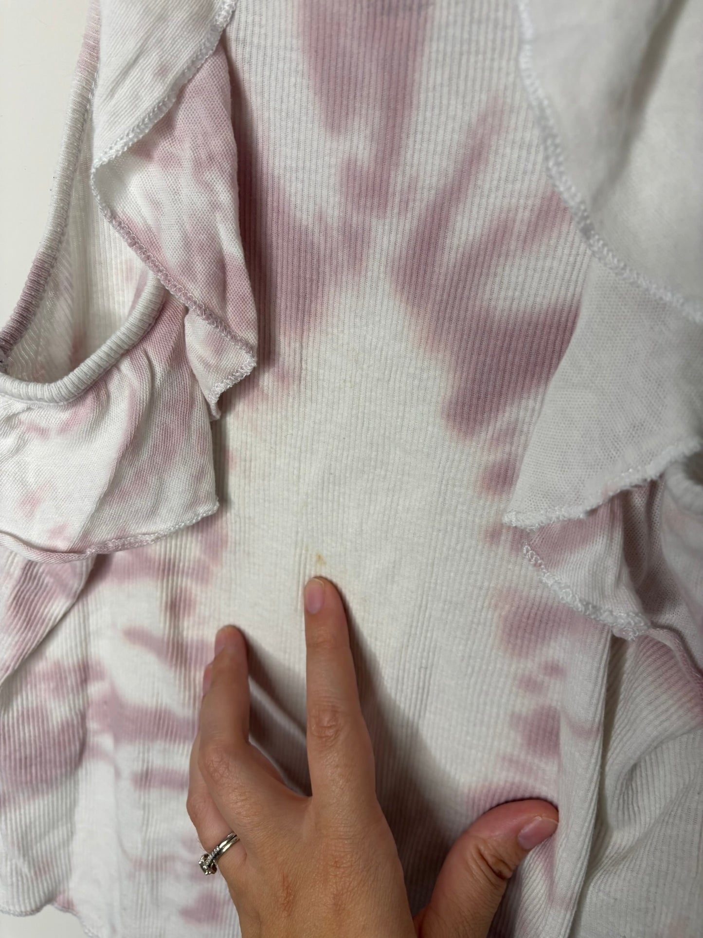 White and pink tie-dye tank top hanging on a black hanger against a brick wall.