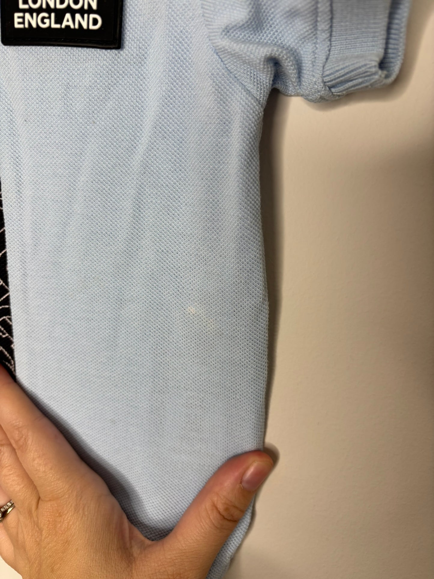 Light blue Burberry London polo shirt with black and white pattern strip and brand logo on the front.