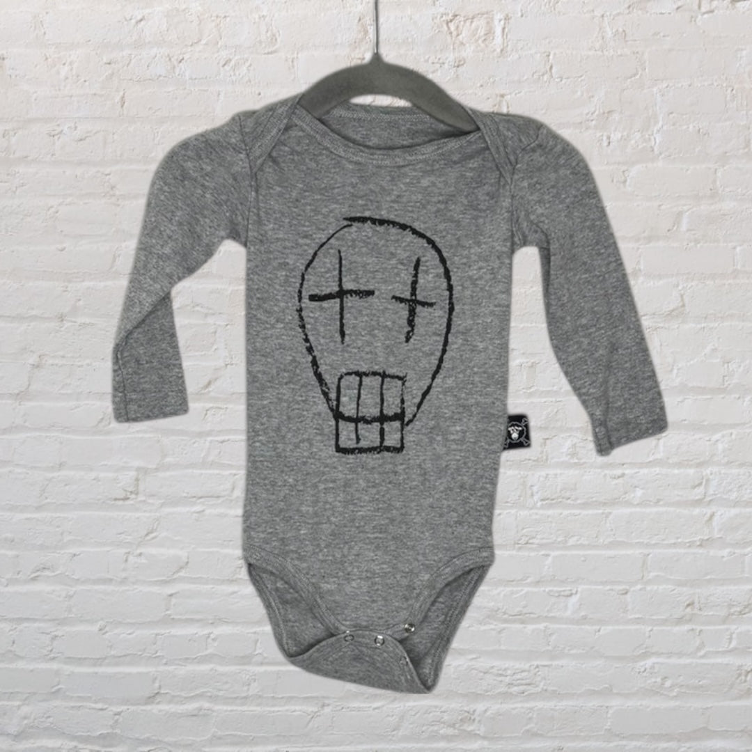 Grey baby bodysuit with long sleeves and a black graphic face design, hanging on a black hanger against a brick wall.