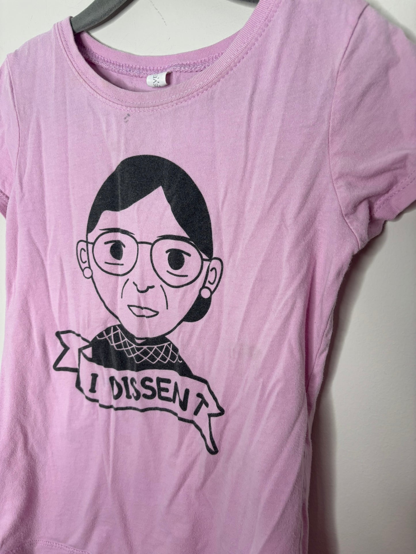 Pink t-shirt with a graphic print of a cartoon character and 'I Dissent' banner.