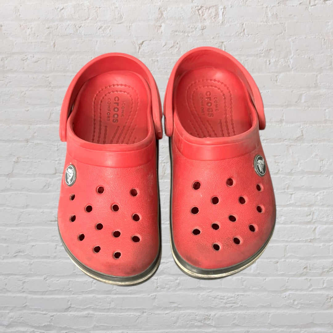 Pair of pink Crocs Classic Clogs with a white and black stripe on the sole, featuring ventilation holes and a strap.