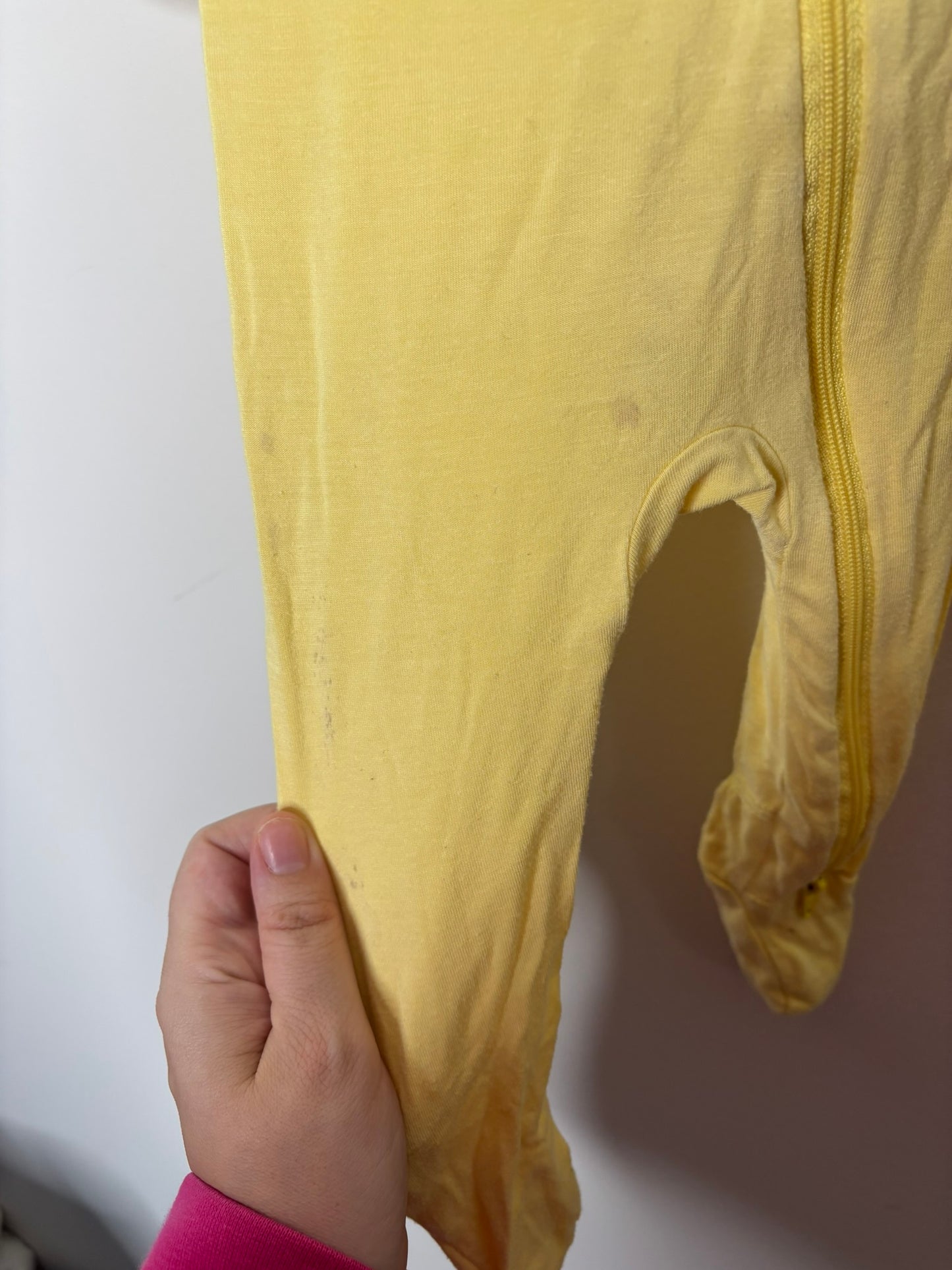 Yellow baby footed sleeper with long sleeves and a front zipper, hanging on a black hanger against a white brick wall.