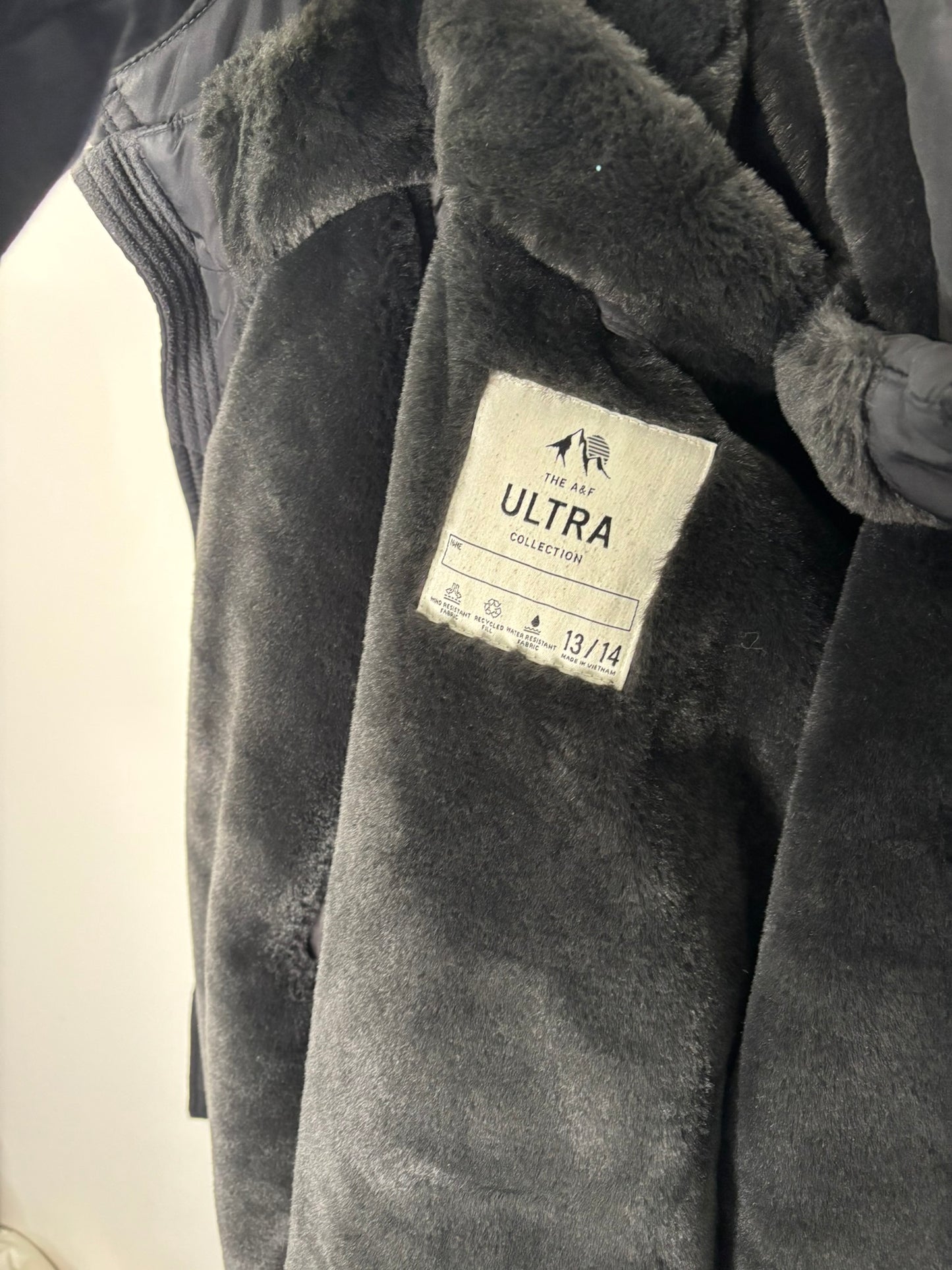 Black puffer jacket with a faux fur hood, hanging against a white brick wall.