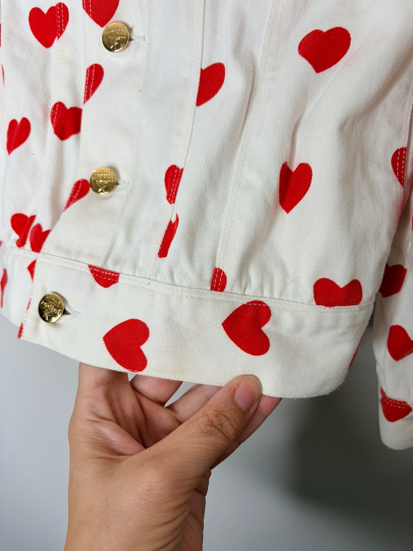 Mini Rodini white denim jacket with red heart prints and gold buttons.
