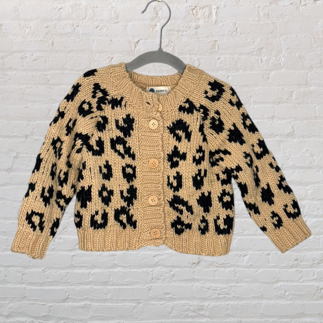 Beige knit cardigan with black leopard print design, button-up front, displayed on a hanger.