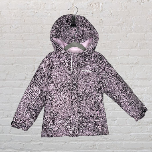 Columbia hooded winter jacket with a purple and black pattern, hanging on a hanger against a white brick wall.