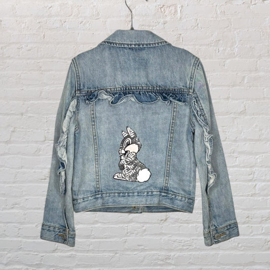 Blue distressed denim jacket featuring a cartoon character patch on the back with frayed details.