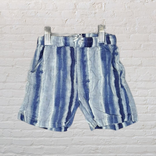 Blue and white tie-dye shorts with elastic waistband, displayed on a hanger against a brick wall.
