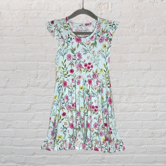 Light blue dress with pink floral print and ruffle sleeves, hanging against a white brick wall.