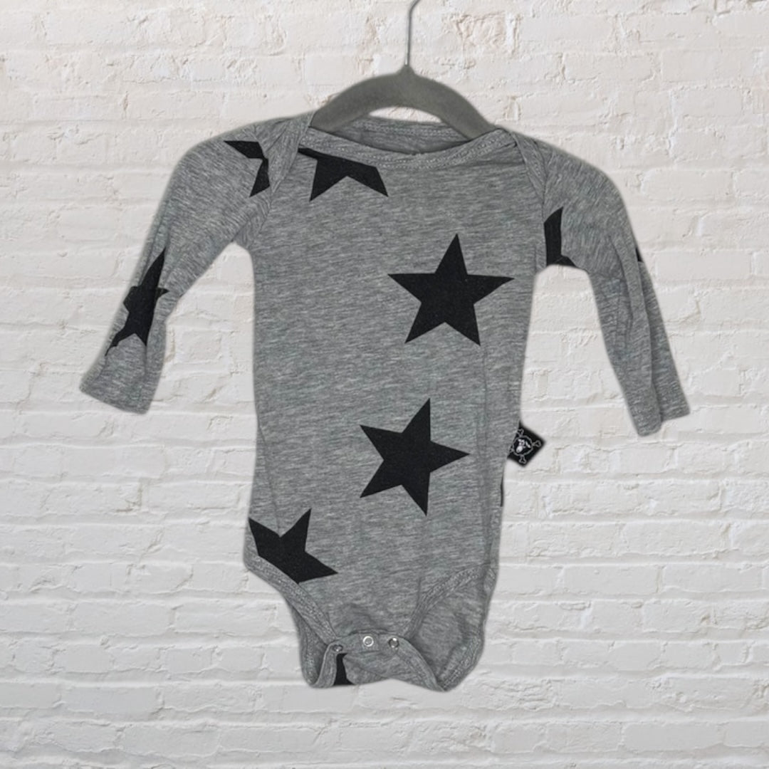 Grey long sleeve baby bodysuit with black star prints, hanging on a black hanger against a white brick wall.