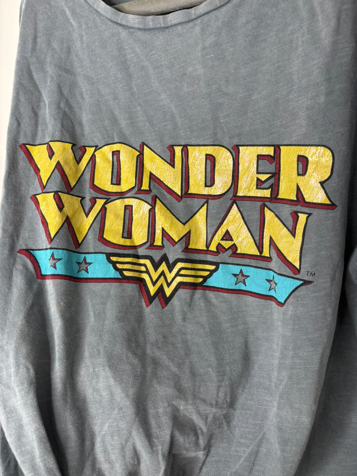Gray Wonder Woman T-Shirt with knot front and colorful logo print, hanging on a hanger.