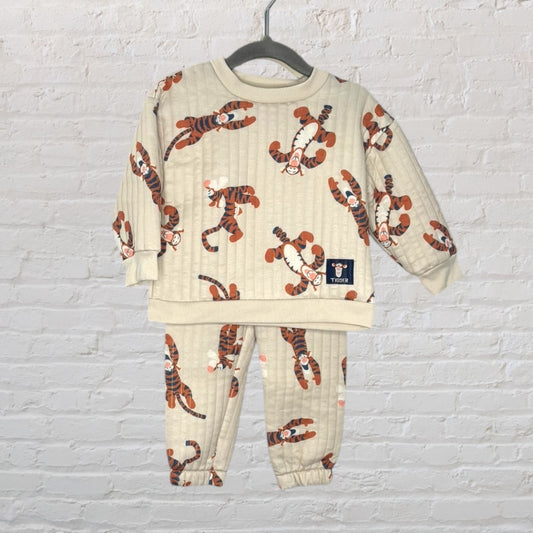 Beige quilted sweatshirt and pants set with Tigger print displayed on a hanger against a white brick wall.