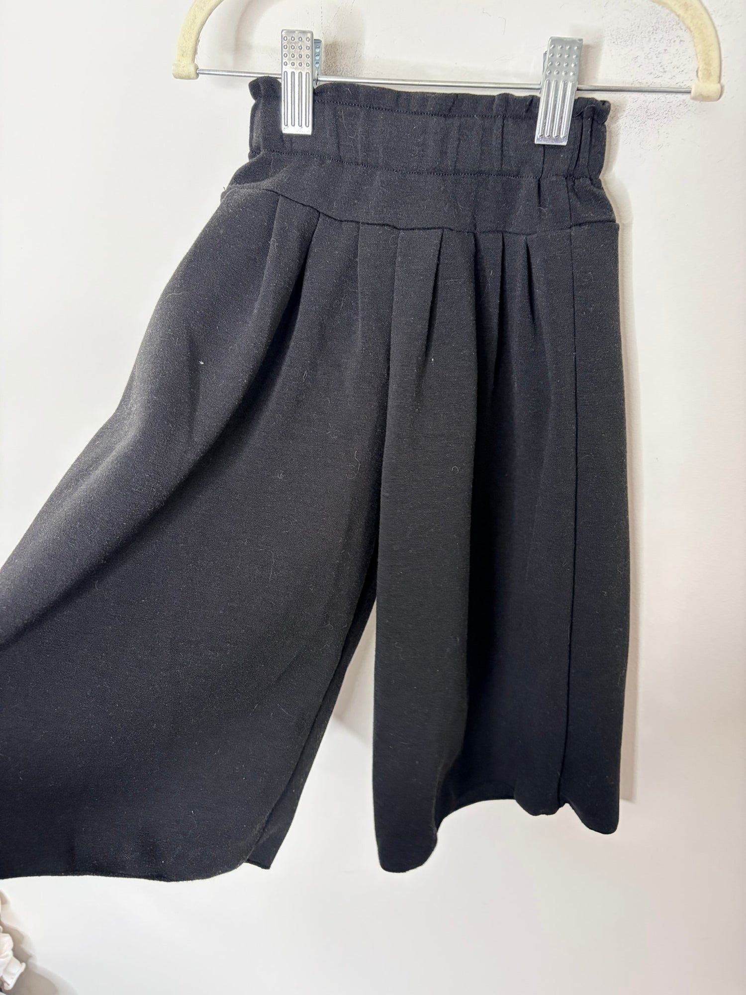Black dress with 3/4 sleeves and a flared skirt, displayed on a hanger against a white brick wall.