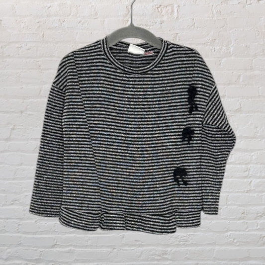 Black and white striped knit sweater with elephant detail on side, hanging on a gray hanger.