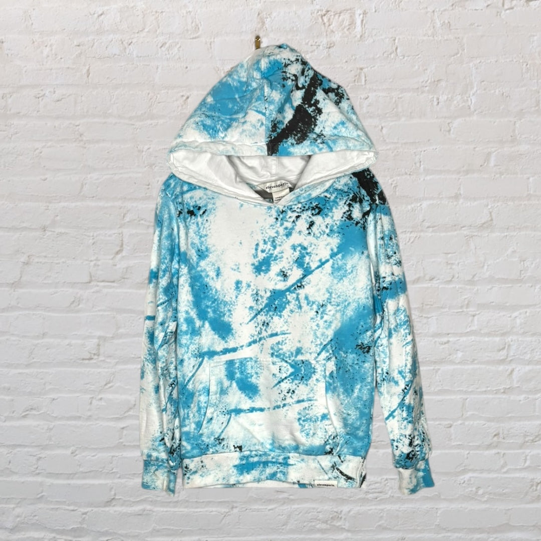 Unisex blue and white tie-dye hoodie with an abstract pattern, hanging on a brick wall.