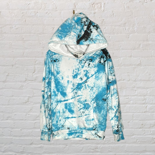 Unisex blue and white tie-dye hoodie with an abstract pattern, hanging on a brick wall.