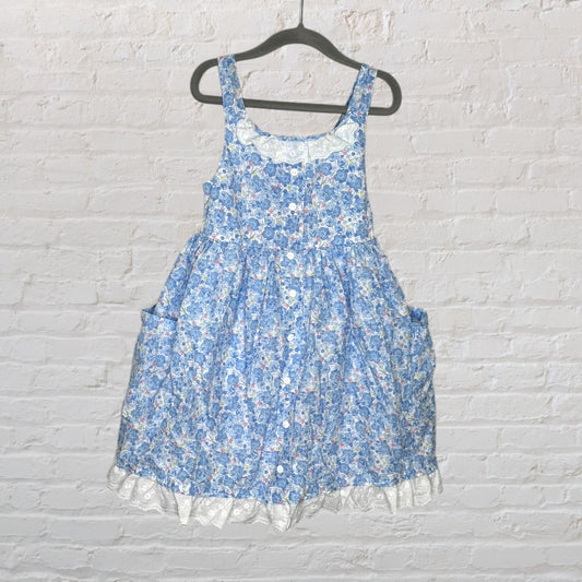 Blue floral sleeveless dress with lace trim details, hanging on a black hanger against a white brick wall.