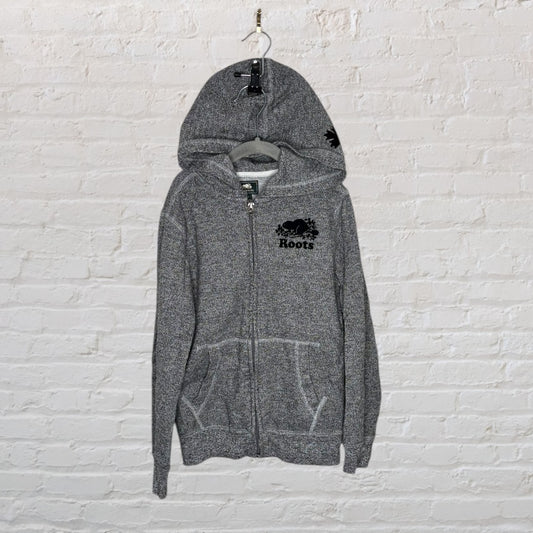 Grey Roots full-zip hoodie with logo, hanging on a brick wall.