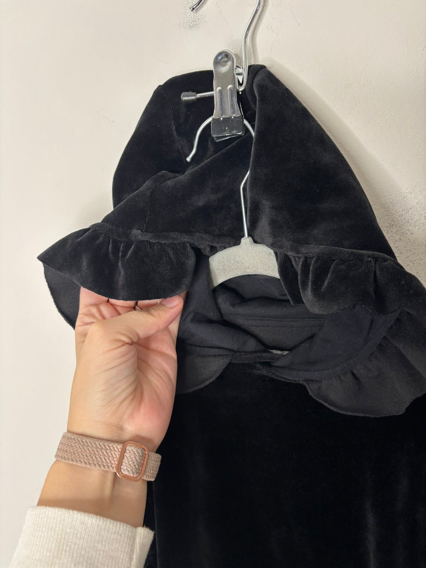 Black velvet dress with a hood and ruffled sides hanging against a white brick wall.