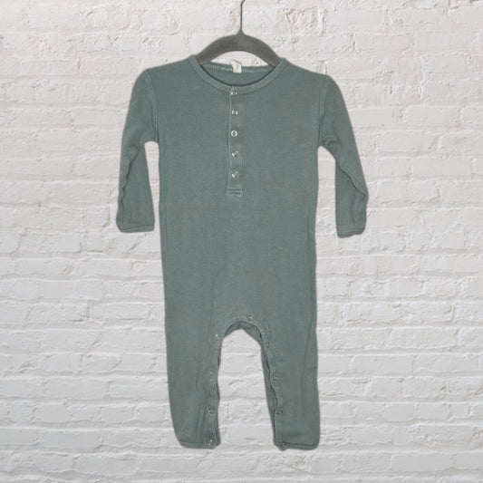 Sage green baby romper with button closure and long sleeves, displayed on a hanger against a white brick wall.