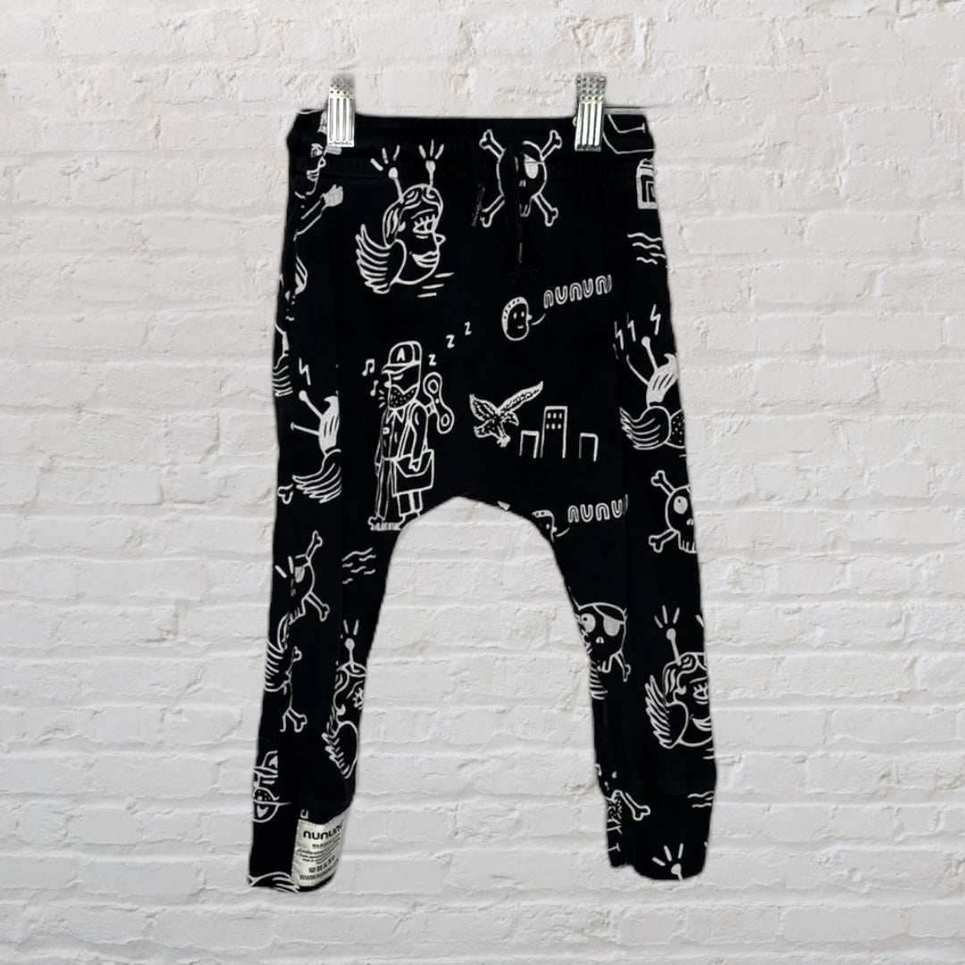 Black harem pants with white doodle print design, displayed against a brick wall.