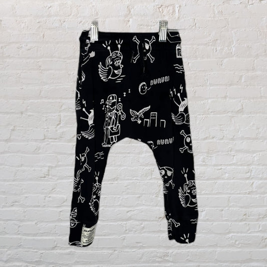 Black harem pants with white doodle print design, displayed against a brick wall.
