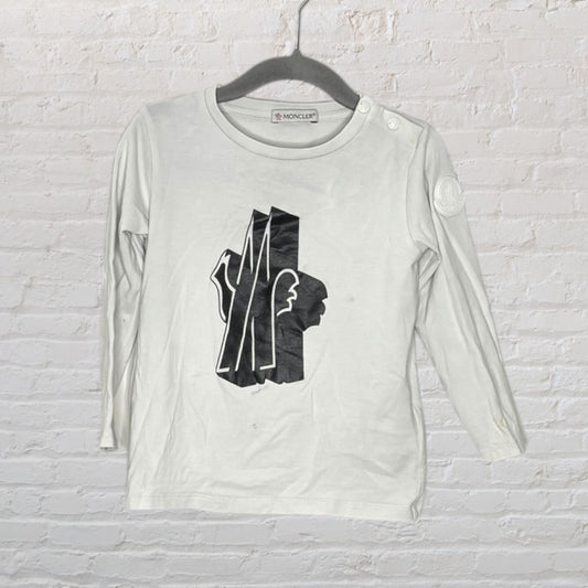 White Moncler long sleeve shirt with black graphic logo on front, hanging on a black hanger.