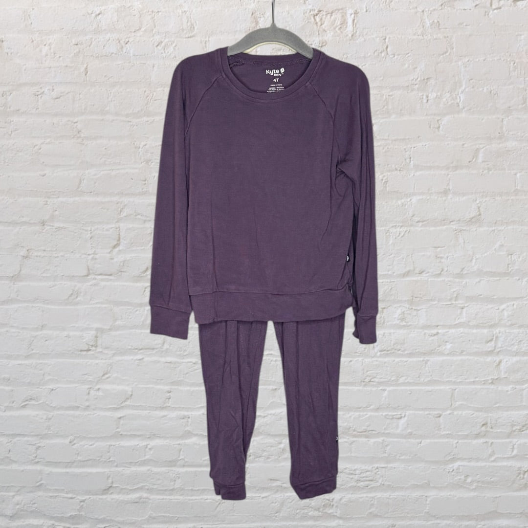 Purple long-sleeve top and pants pajama set for kids by Kyte, size 4T, displayed on a hanger against a brick wall.