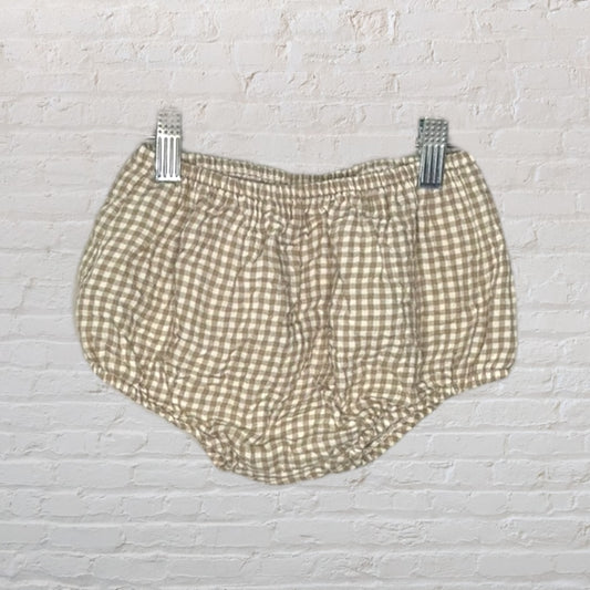 Brown and white gingham checkered baby bloomers with elastic waistband displayed against a brick background.