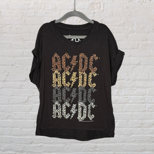 Black T-shirt with leopard print AC/DC graphic design, hanging on a hanger against a white brick background.