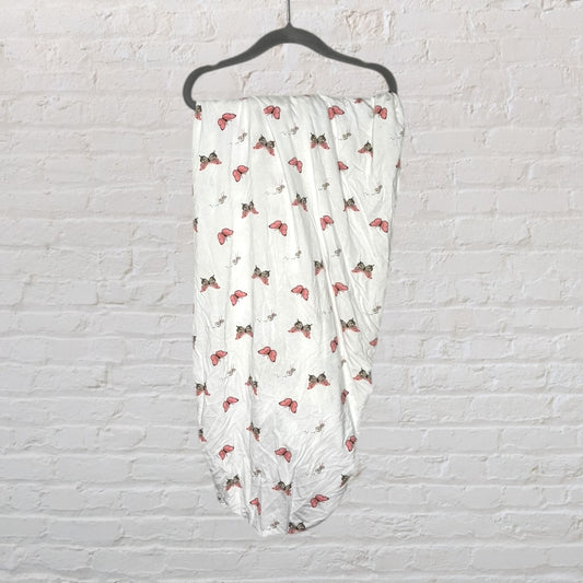 White cotton swaddle blanket with pink and brown butterfly prints hanging on a black hanger against a brick wall.
