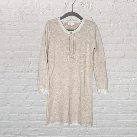Beige knit dress with long sleeves and button detail on the front, hanging on a black hanger against a white brick wall.