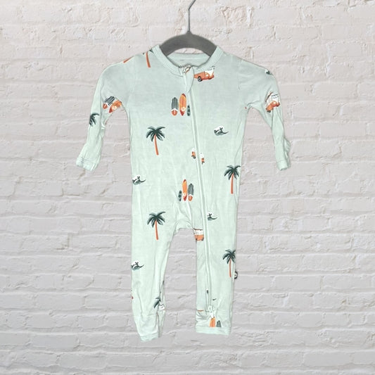 Light green baby onesie with palm tree, surfboard, and car print, featuring a zipper closure, hanging against a brick wall.