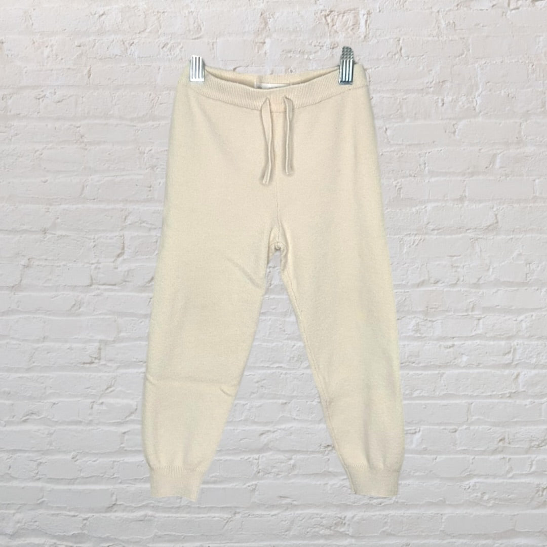 Cream-colored knit sweater and pants set hanging on a hanger against a white brick wall.