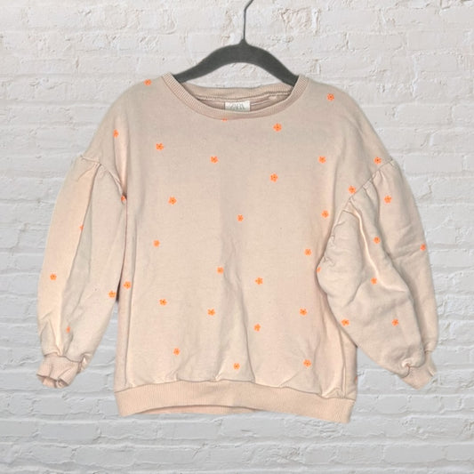Light pink sweater with orange floral embroidery and puff sleeves, hanging on a black hanger.
