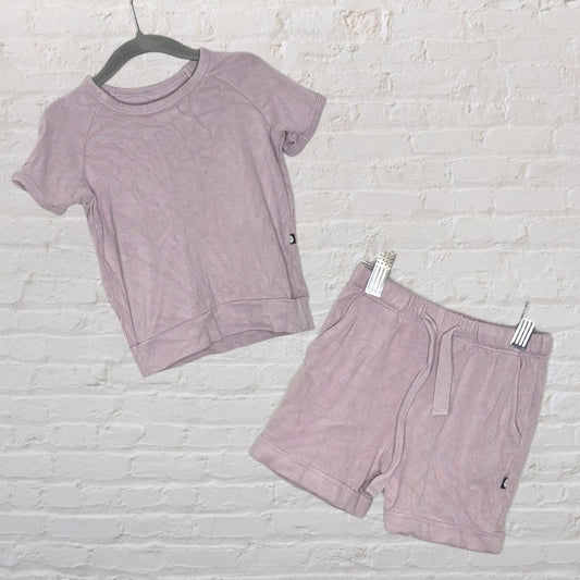 Two-piece lounge set in light lavender, featuring a short-sleeve top and matching shorts, displayed against a brick wall.