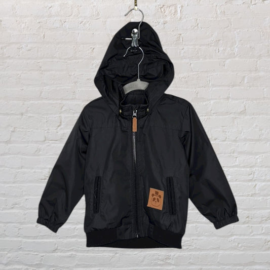 Black hooded outerwear jacket with front zipper and a brown patch on the lower side, hanging on a hanger.