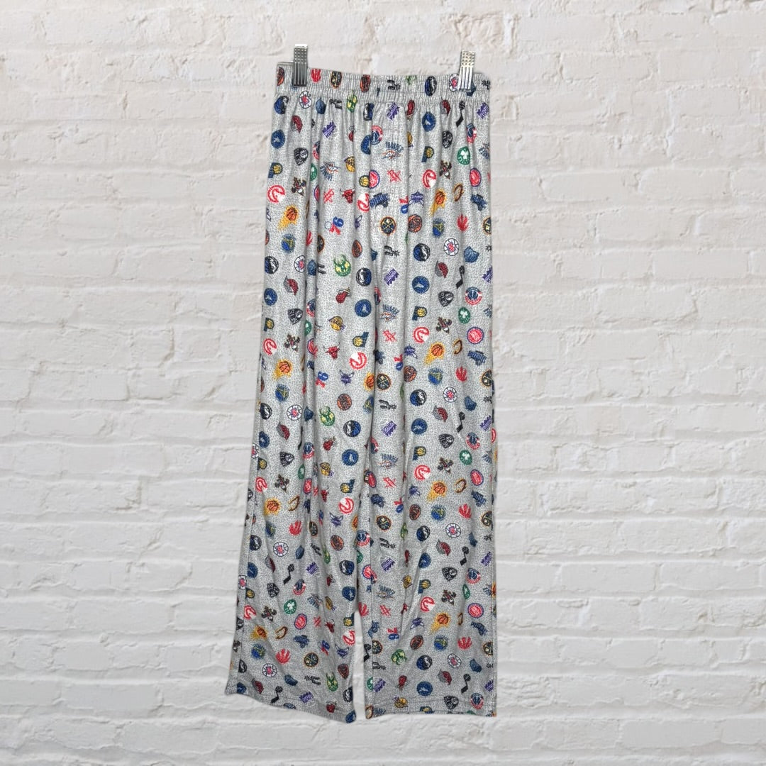 Grey lounge pants with a colorful sports-themed pattern displayed against a white brick background.