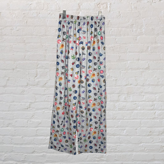 Grey lounge pants with a colorful sports-themed pattern displayed against a white brick background.