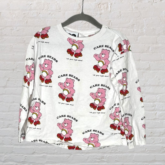 White long sleeve shirt featuring a repeating print of pink Care Bears with the text 'Let your light shine!'