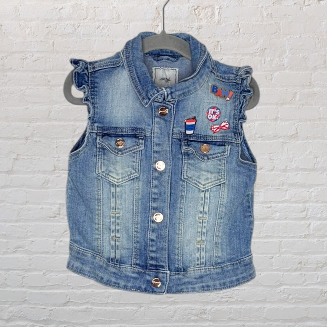Blue denim sleeveless vest with decorative patches and button closure, hanging on a hanger.