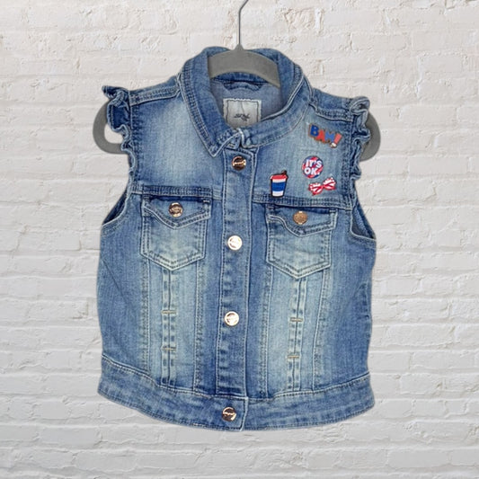 Blue denim sleeveless vest with decorative patches and button closure, hanging on a hanger.