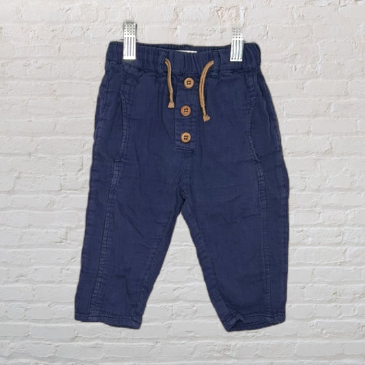 Navy blue kids' pants with button closure and drawstring, hanging on clips against a white brick background.