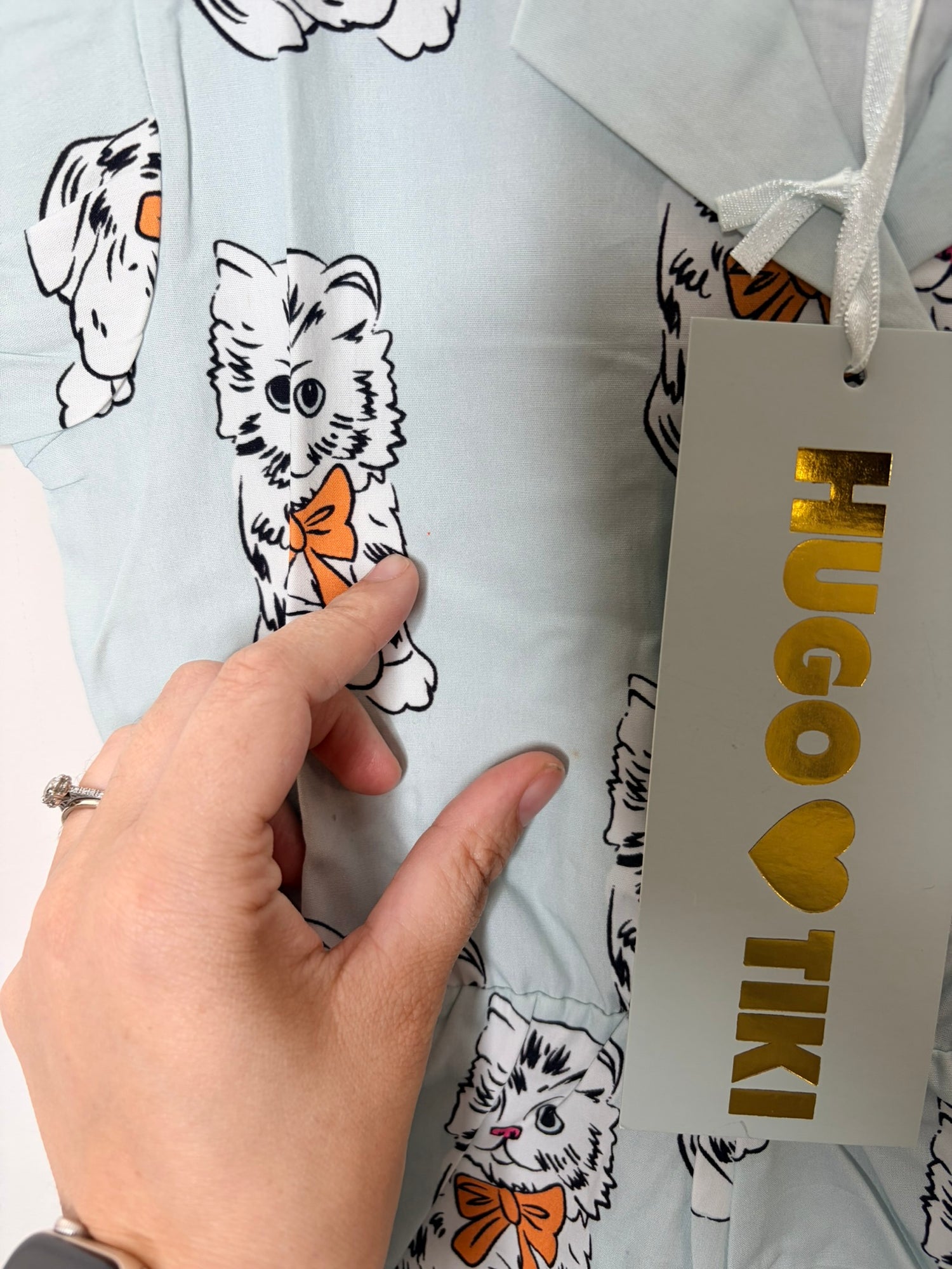 Light blue romper with cat print and ruffle sleeves by Hugo Loves Tiki, hanging on a hanger with a tag attached.